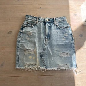 Jeanskjol - Säljer en ljusblå jeanskjol från FB Sister i storlek XS. Kjolen har slitna detaljer, fransig nederkant och klassiska fickor både fram och bak.
