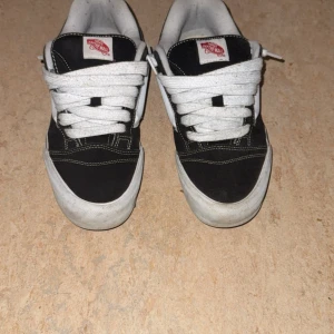Svarta och vita Vans Old Skool sneakers - Klassiska Vans Old Skool sneakers i svart och vitt med vit sula och ikonisk sidostrip. Skorna har snörning, rund tå och är tillverkade i mocka och textil. Perfekta för en streetwear-look och passar till det mesta i garderoben.