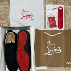 Christian Louboutin svarta sneakers mocka - Svarta sneakers från Christian Louboutin i lyxig mocka med ikonisk röd sula och diskret logga. Skorna har rund tå, svarta snören och stilren design som sticker ut med den klassiska röda undersidan.