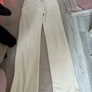 Beiga mjukisbyxor Juicy Couture S - Beiga mjukisbyxor från Juicy Couture i storlek S. Byxorna har raka ben, bred resår i midjan med snörning och stora fickor både fram och bak. Mjukt och skönt material som känns lyxigt och chill. Lite fläckar på bena 