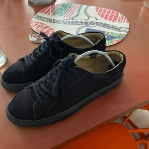 Myrqvist mocca sneakers - Stilrena svarta sneakers i mocka med klassisk rund tå och platt sula. Skorna har svarta skosnören och diskreta sömmar för en clean look. Perfekta för dig som gillar minimalistisk stil och vill ha ett par bekväma skor till vardags.