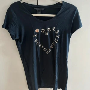 Mörkblå Marc by Marc Jacobs T-shirt - Mörkblå t-shirt från Marc by Marc Jacobs med coolt tryck i form av ett hjärta och text på bröstet. Klassisk rund halsringning och korta ärmar. Perfekt för dig som gillar stilrena statement-plagg