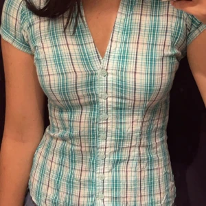 Rutig kortärmad skjorta från Amisu - Säljer en snygg rutig skjorta från Amisu i storlek XS. Skjortan har ett mönster i turkos, svart och vitt med korta ärmar och knappar framtill. Lite y2k