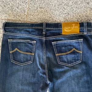 Blå jeans från Jacob Cohen - Snygga blå jeans från Jacob Cohen med klassisk design och kontrasterande sömmar. Tillverkade i Italien med högkvalitativt denimtyg. Perfekta för en stilren look. Längden på byxorna är 110cm, och det är W34. Detta är en limiterad utgåva köpt på Stenströms för något år sedan, och har inte kommit till den användning jag trodde de skulle! 