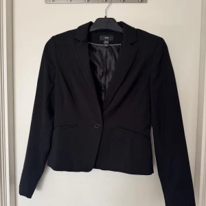 Svart kavaj  - Snygg svart kvinno kavaj med knapp i mitten samt knappar längst ned på ärmarna för en snygg detalj. 