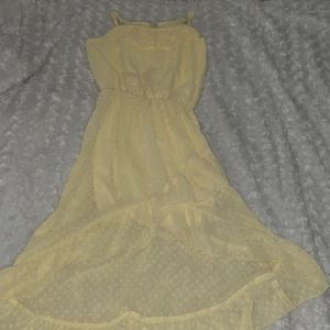 Gul ärmlös klänning med volang - Söt gul klänning med prickigt mönster och volangdetaljer. Klänningen är ärmlös och har en elastisk midja för en bekväm passform. Perfekt för somriga dagar!💛🤍