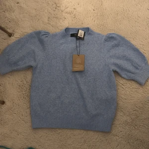 Ljusblå tröja från Vero Moda - Säljer en ljusblå tröja från Vero Moda med puffiga ärmar och ribbade muddar. Tröjan är tillverkad av återvunnen polyester och har en mjuk och bekväm känsla. Perfekt för en stilren look.