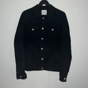 Svart jeansjacka från Jack & Jones - Snygg svart jeansjacka från Jack & Jones med silverfärgade knappar. Jackan har en klassisk design med två bröstfickor och långa ärmar. Perfekt för en stilren look.