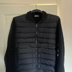 Marinblå jacka från Moncler - Snygg marinblå jacka från Moncler med dragkedja och quiltad design på framsidan. Jackan har långa ärmar och en stilren look, perfekt för kyligare dagar. NFC Tagg på logga. Passar L samt XL