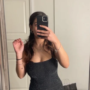 Svart glittrig klänning - Säljer en elegant svart glittrig klänning med smala axelband. Klänningen har en tight passform som framhäver figuren och är perfekt för festliga tillfällen. Den gnistrar vackert i ljuset och ger en glamorös känsla.