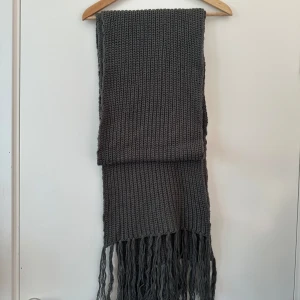 Grå stickad halsduk från ONLY - Säljer en snygg grå stickad halsduk från ONLY med långa fransar i ändarna. Perfekt för att hålla dig varm under kyliga dagar. Den är mjuk och bekväm att bära.