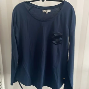 Mörkblå långärmad tröja från Hampton Republic - Säljer en stilren mörkblå långärmad tröja från Hampton Republic. Tröjan har en liten bröstficka och rund halsringning. Perfekt för en avslappnad look. Passar bra till jeans eller chinos.