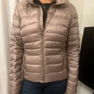 Beige dunjacka med dragkedja - Säljer en stilren beige dunjacka med dragkedja. Jackan har en normal passform och är perfekt för kyligare dagar. Den quiltade designen ger ett modernt utseende och den har långa ärmar för extra värme.