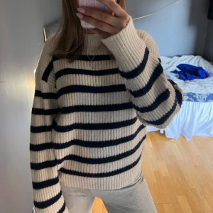 Randig stickad tröja - Säljer en mysig randig stickad tröja i vit och svart. Tröjan har en ribbad struktur och långa ärmar.