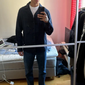 Mörkblå overshirt - Säljer en stilren mörkblå overshirt med knappar framtill. Jackan har en klassisk krage och långa ärmar. Perfekt för lager-på-lager-stil. Linne overshirt från massimodutti helt oanvänd. Perfekt till sommar med linne byxor eller andra snygga outfits att kombinera!