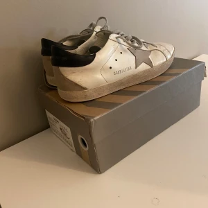 Vita sneakers med stjärndetalj - Snygga vita sneakers från GGDB med en grå stjärndetalj på sidan och svart häl. Bra skick! Pris kan diskuteras! Kan köpas i bundle för billigare pris! 
