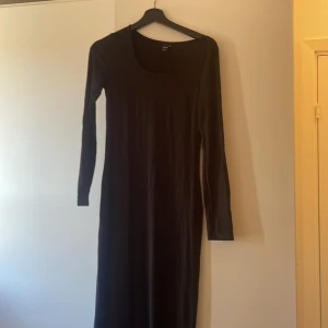 Svart långklänning - Elegant svart långklänning med långa ärmar. Perfekt för en stilren look. Klänningen har en enkel design som gör den lätt att matcha med olika accessoarer.