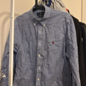 Blårutig skjorta från Ralph Lauren - Säljer en stilren blårutig skjorta från Ralph Lauren i slim fit. Skjortan är tillverkad i 100% bomull och har en broderad logotyp på bröstet. Perfekt för en klassisk och tidlös look.