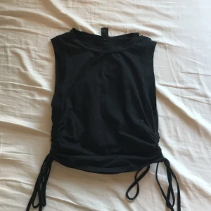 Svart ärmlös topp från Shein - Snygg svart ärmlös topp från Shein med knytband i sidorna för en justerbar passform. Perfekt för en stilren look.💞