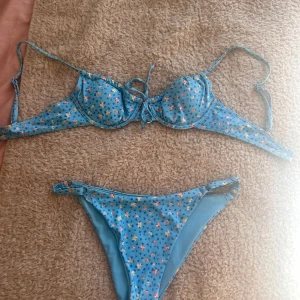 Blå blommig bikini - Snygg blå bikini med blommigt mönster och knytning fram. Perfekt för sommarens stranddagar. Toppen har justerbara axelband och bygel för extra stöd.
