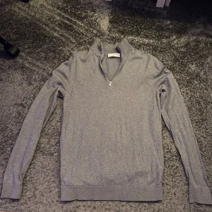 Half zip  - Säljer en stilren grå tröja från Selected Homme. Tröjan har en praktisk dragkedja vid halsen och är tillverkad i ett mjukt material. Perfekt för en avslappnad men snygg look.
