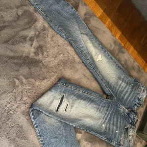 Blå jeans med slitningar - Snygga blå jeans med coola slitningar och en klassisk femficksdesign. De har en dragkedja och knapp framtill. Perfekta för en avslappnad stil.
