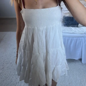 Vit ärmlös klänning - Säljer en söt vit klänning med smockdetaljer upptill och tunna axelband. Kjolen är luftig och har en lätt volangstil. Perfekt för varma dagar! Den är ursprungligen från zara men köpt den här på plick innan! Skriv vid frågor och funderingar!💕