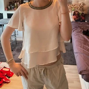 Zara blus med strass  - Säljer en elegant vit blus med korta ärmar och dubbla lager. Blusen har en vacker strassning runt halsringningen. Från Zara, XS. Finns knapp som man sätter i där bak, kunde inte göra det själv på bilden dock så höll upp den ist 😅 