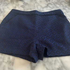 Blå mönstrade shorts - Snygga blå shorts med ett geometriskt mönster i mörkare nyans. De har en dragkedja bak och en stilren design som passar perfekt för en trendig look.