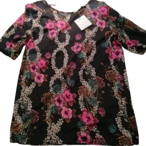 Blommig klänning från Sandro - Snygg klänning från Sandro med ett färgglatt blommönster i rosa, grönt och brunt på en svart bakgrund. Klänningen har korta ärmar och en v-ringad design. Perfekt för att lysa upp garderoben!