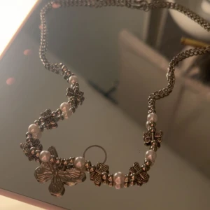 Halsband med fjäril och pärlor - Charmigt halsband med en stor fjärilsberlock i silverfärg. Kedjan är dekorerad med små blommor och vita pärlor som ger en elegant touch. Perfekt för alla🩷Ordinarie pris 89kr
