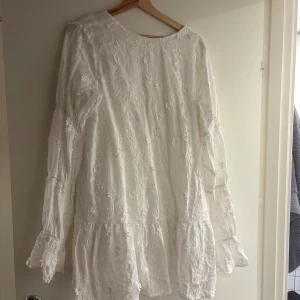 Vit långärmad klänning med spetsdetaljer - Charmig vit klänning med långa ärmar med blommor ish på. Perfekt för studenten eller likande. Klänningen har en luftig passform och är idealisk för vår och sommar. Den är från NAKD, den blev viral för ett par år sedan 🥰