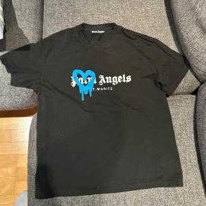 Svart t-shirt från Palm Angels - Säljer en svart t-shirt från Palm Angels med ett coolt blått hjärta och text på framsidan.