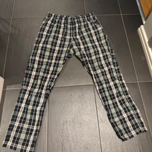 Rutiga bomullsbyxor i loose fit - Snygga rutiga byxor i mörkblått, vitt och grått med inslag av lila. De har en relaxed loose fit, elastisk midja och raka ben. Perfekta för chill dagar eller när du vill ha en avslappnad stil. Tillverkade i mjuk bomull för extra komfort.