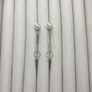Långa silverörhängen med pärldetalj och spetsig hängande del - Säljer ett par stilrena örhängen i silverfärg med stor vit pärla upptill och kedjor som avslutas med en lång spetsig, konformad detalj. Perfekta för dig som gillar modern och edgy design.