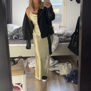 Guldig Satinklänning - Säljer min guldiga Satinklänning med korsade band i ryggen. Banden knyter man själv och kan därför justera storleken. Perfekt till sommaren eller balen! Endast använd vid ett tillfälle på bankett🥳så väldigt bra i skicket!