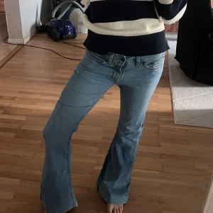 Ljusblå bootcut jeans - Säljer ett par ljusblå bootcut jeans med klassisk femficksdesign och låg midja. Jeansen har en lätt utsvängd passform nertill och stängs med dragkedja och knapp. Perfekta för dig som gillar en retroinspirerad stil.