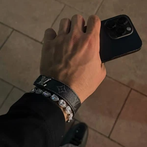 Svart armband från Louis Vuitton - Säljer ett svart armband från Louis Vuitton med klassiskt monogrammönster och ett stort LV-spänne i metall. Bältet har en lyxig känsla och är tillverkat i skinn med tydliga vita detaljer.