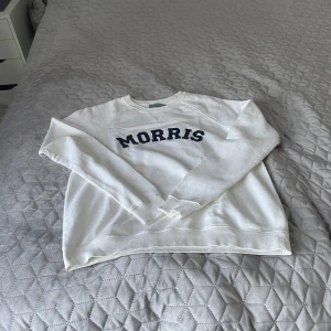 Vit sweatshirt från Morris Lady - Vit sweatshirt från Morris Lady med mörkblå text på bröstet. Klassisk rund halsringning och långa ärmar. Mjuk bomullskvalitet och ribbade muddar vid ärmslut och nederkant. Perfekt för en avslappnad och stilren look.