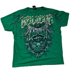 Grön t-shirt med tryck från Tapout - Säljer en grön t-shirt från Tapout med stort grafiskt tryck och texten 'Believe Tapout' på framsidan. T-shirten har korta ärmar och är tillverkad i bomull. Perfekt för dig som gillar sportiga och tuffa plagg.