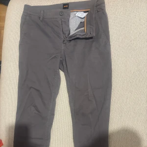 Grå chinos från Boss - Boss orange collection, Snygga grå chinos från Boss med klassisk passform och diskreta fickor fram och bak. Byxorna har dragkedja och knapp i midjan samt stilren design som passar till många tillfällen.