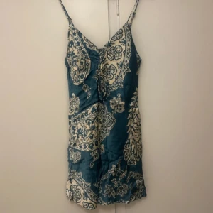 Mönstrad klänning Zara - Säljer en kort klänning med smala axelband ifrån Zara. Klänningen har ett dekorativt mönster och knytning framtill vid bysten. Perfekt för sommardagar eller när du vill känna dig extra fin.