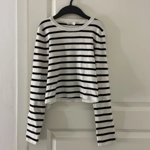 Randig långärmad tröja från Gina Tricot - Säljer en vit långärmad tröja med svarta horisontella ränder från Gina Tricot. Tröjan har en croppad passform och rund halsringning. Perfekt till vardags för en stilren och avslappnad look.