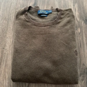 Brun ulltröja från Polo Ralph Lauren - Säljer en klassisk brun tröja från Polo Ralph Lauren i mjuk ull. Tröjan har rund halsringning och diskret mönster i tyget. Perfekt för lager-på-lager och snygg till både jeans och chinos.