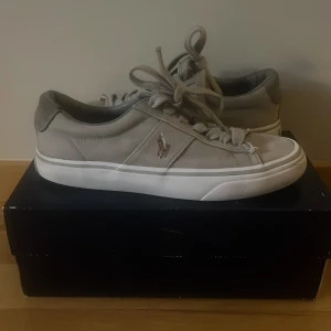 Polo Ralph Lauren skor - Snygga grå sneakers från Polo Ralph Lauren med vit sula och klassisk logga på sidan. Skorna har snörning och rund tå, perfekt för en stilren vardagslook. Box ingår