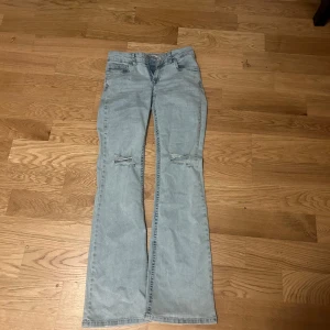 Ljusblå bootcut jeans med broderade bakfickor - Säljer ett par ljusblå bootcut jeans med slitningar vid knäna och snygga broderade detaljer på bakfickorna. Jeansen har klassisk femficksdesign och låg midja. 