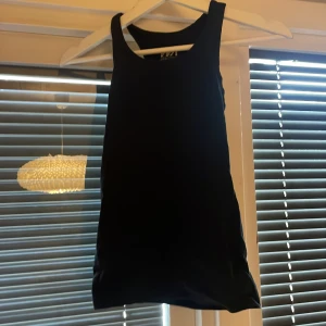 Svart ärmlös klänning från WA Action Sports - Säljer en svart, ärmlös klänning från WA Action Sports. Linne har en sportig design med rund halsringning och tight passform. Perfekt för dig som gillar en enkel och stilren look.