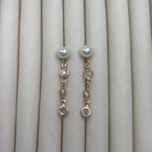 Guldiga örhängen med pärlor och stenar - Säljer ett par eleganta örhängen i guldton med vita pärlor upptill och hängande klara stenar. Perfekta för att lyfta din look med en touch av lyx och stil.