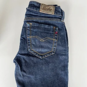 Replay blå jeansbyxor med raka ben - Snygga blå jeans från Replay med raka ben och klassiska gula sömmar. Byxorna har fem fickor, knappgylf och tydlig Replay-logga på bakfickan. Perfekta för dig som gillar en tidlös jeanslook.