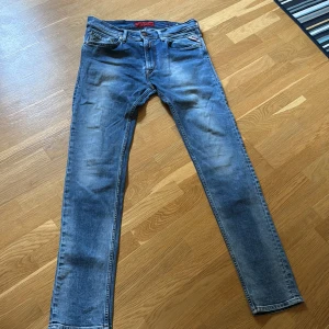 Replay Jondrill jeans i blå denim - Säljer ett par Replay Jondrill jeans i klassisk blå tvätt med lätt slitningar. Jeansen har smal passform, fem fickor och dragkedja. Perfekta för dig som gillar en modern och stilren look.